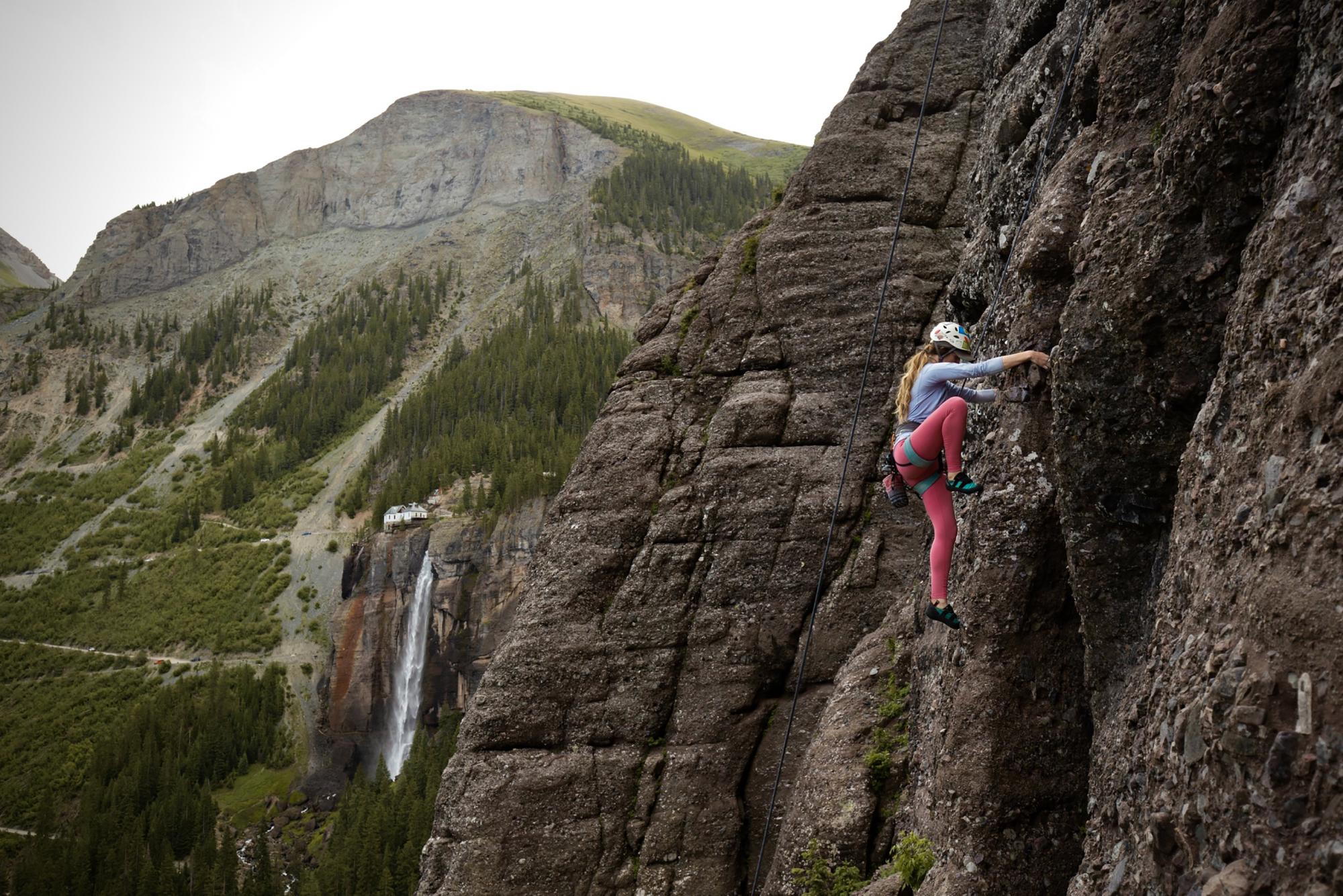 Photo of a person rock climbing by surrounding mountains and waterfall